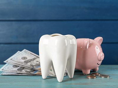 A ceramic model tooth next to some money and a pink piggy bank
