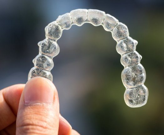Hand holding an Invisalign clear braces tray
