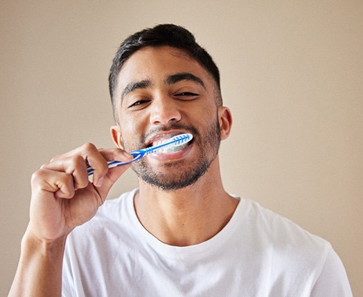 A handsome young man brushing his teeth in front of a bathroom mirror