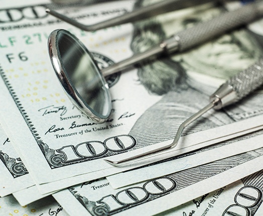 Dental tools lying on a pile of hundred-dollar bills