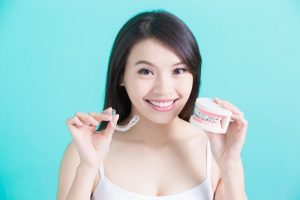 a woman holding Invisalign braces and a mold of traditional braces