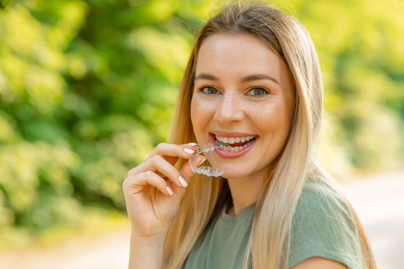 A smiling woman with freckles holding an Invisalign tray