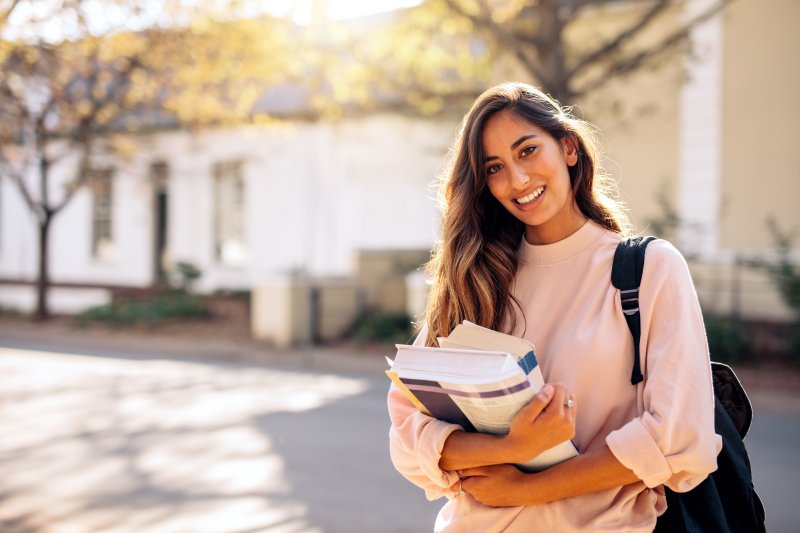 A smiling student carrying textbooks