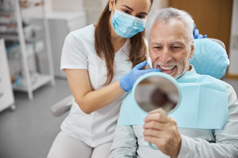 An aging man admiring his new dental implants in a hand mirror