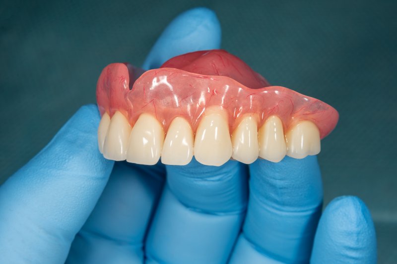 A closeup of a gloved hand holding a denture