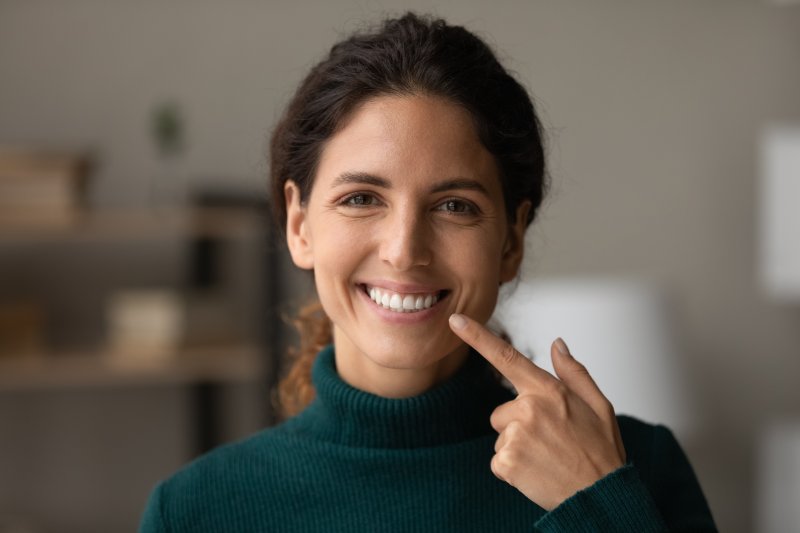 A smiling woman pointing to her beautiful teeth