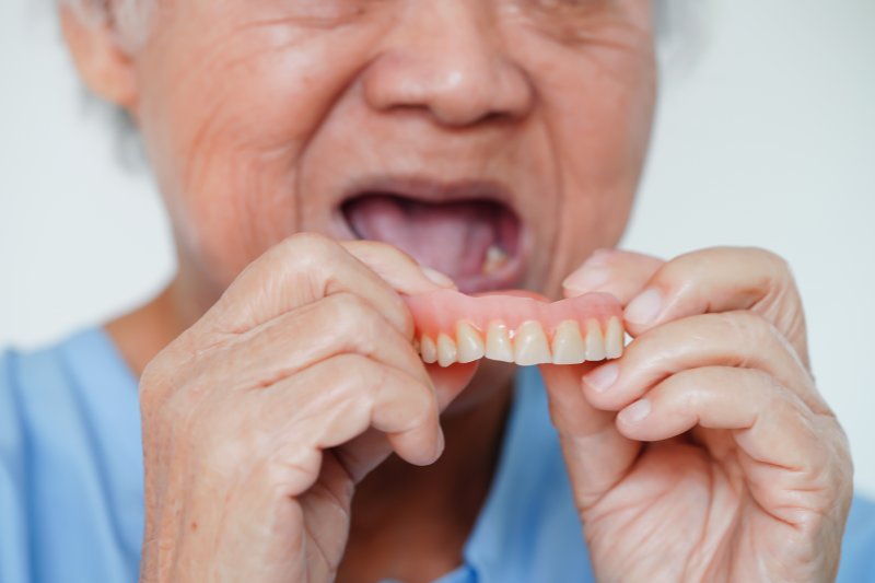 A senior woman about to put ill-fitting dentures in her mouth